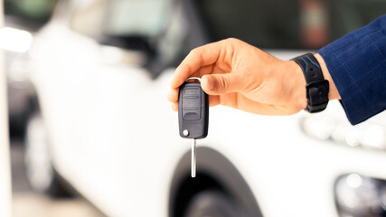 Unrecognizable businessman hand with key from brand new auto, standing over luxury white car,...