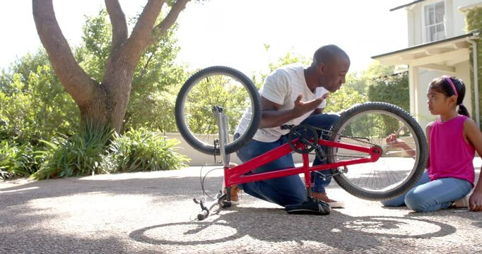 Fixing bicycle, African american man teaching girl how to repair bike outdoors