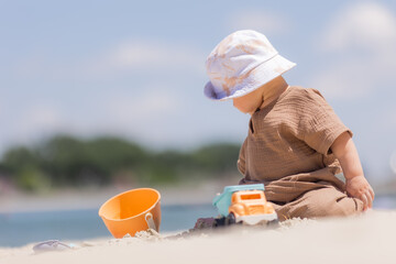 toddler boy plays on a sandy beach in a panama hat and cotton clothes in summer
