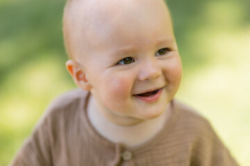 Baby boy walks barefoot on the lawn in summer, children's muslin suit
