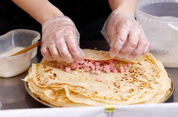 A person is making a ham and cheese pastry