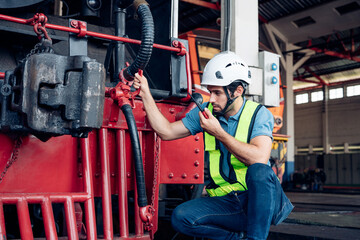 Male engineer worker maintenance locomotive engine wearing safety uniform, helmet and gloves in locomotive repair garage. Maintenance cycle concept.