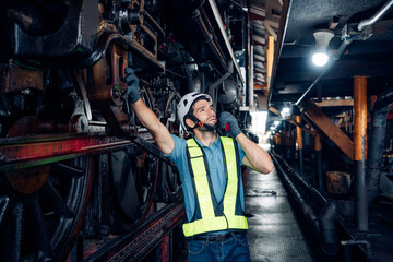 Male engineer worker maintenance locomotive engine wearing safety uniform, helmet and gloves in locomotive repair garage. Maintenance cycle concept.