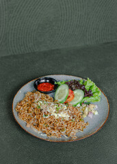 Fried Noodles With Pickles, Vegetables, And Chili Sambal On A Plate, Flavorful And Spicy Dish Served Fresh.