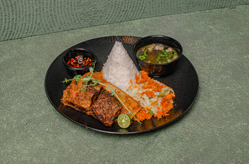 Grilled Ribs Served With Rice, Fresh Salad, A Bowl Of Soup, And Sweet Soy Sambal On A Black Plate, A Flavorful, Tasty, And Satisfying Meal.