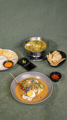 Rice Cake Curry With Satay And Egg, Served With A Bowl, A Plate Of Rice, A Bowl Of Beef Soto, Garnished With Sambal, And Crackers.