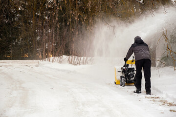 A man removes snow along the road with a yellow snowblower, copy space.