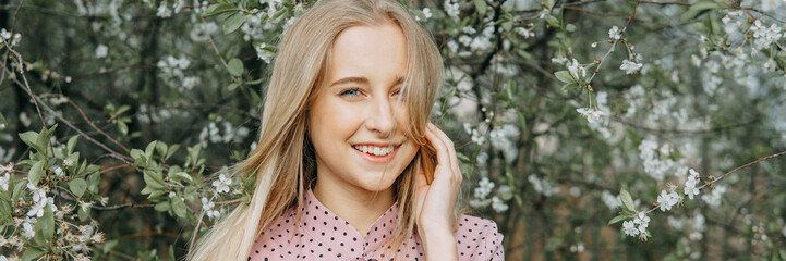 Blonde girl on a spring walk in the garden with cherry blossoms. Female portrait, close-up. A girl in a pink polka dot dress.
