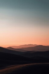 Fototapeta premium Sunset over mountains with a vibrant sky and clouds, casting an orange glow on the hills and desert landscape