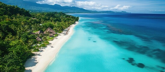 Tropical paradise with turquoise waters gently lapping a white sandy beach, lush green vegetation, and distant mountains under a bright blue sky.