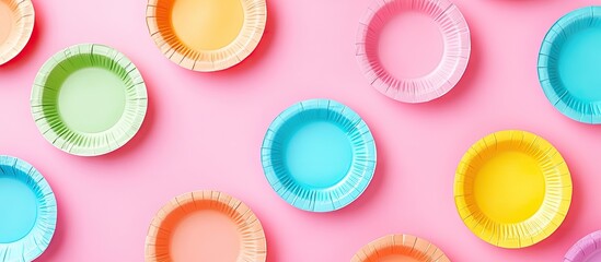Colorful paper plates in pastel shades of green, blue, yellow, and peach arranged on a soft pink background, creating a vibrant party theme.