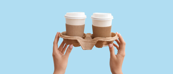 Female hands with takeaway paper cups and holder on blue background