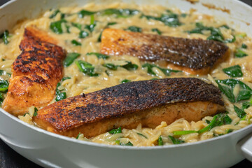 Close-up of a cooked salmon filet with orzo pasta and spinach in a white pan, showcasing a healthy and delicious meal