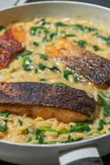 Close-up of a cooked salmon filet with orzo pasta and spinach in a white pan, showcasing a healthy and delicious meal