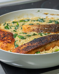 Close-up of a cooked salmon filet with orzo pasta and spinach in a white pan, showcasing a healthy and delicious meal