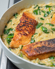 Close-up of a cooked salmon filet with orzo pasta and spinach in a white pan, showcasing a healthy and delicious meal
