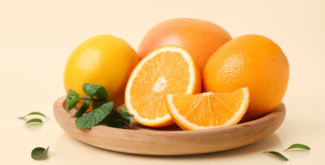 Wooden plate with ripe citrus fruits on beige background
