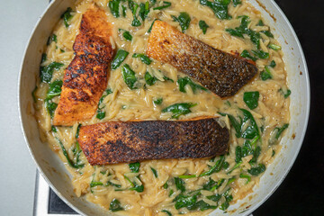 Close-up of a cooked salmon filet with orzo pasta and spinach in a white pan, showcasing a healthy and delicious meal