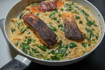 Close-up of a cooked salmon filet with orzo pasta and spinach in a white pan, showcasing a healthy and delicious meal