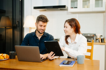Modern couple collaborating over coffee in a cozy kitchen setting with a laptop, notebook, and breakfast.