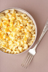 Bowl of tasty Italian pasta with Cheddar cheese on beige background, closeup