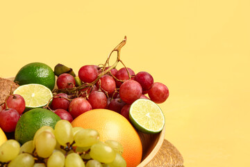 Bowl with different fresh fruits on orange background