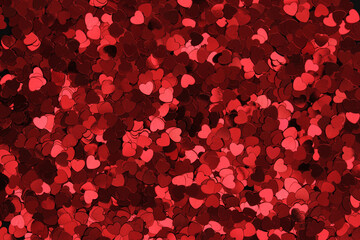 Red glittery heart shaped confetti on a black backdrop. Background pattern.