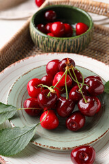 Plate and bowl with sweet cherries on wicker tray, closeup