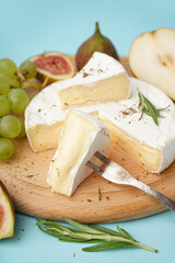Wooden board with pieces of tasty Camembert cheese on blue background