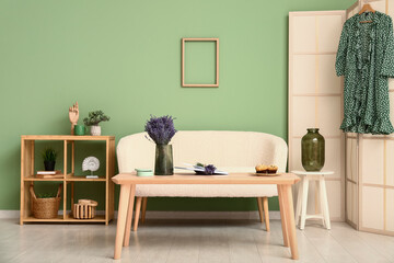 Interior of stylish living room with folding screen, shelving unit, sofa, table and beautiful lavender flowers