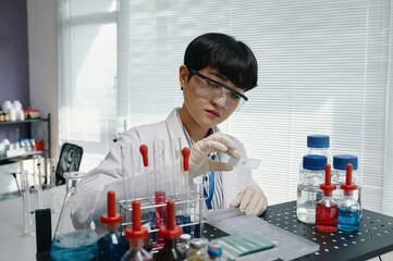 Scientist conducting laboratory experiment involving chemical samples and glassware setup in...