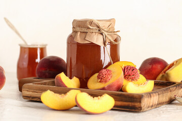 Jar with sweet peach jam and fresh fruits on light background
