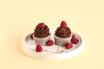 Plate of tasty chocolate cupcakes with raspberries on beige background