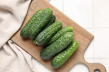 Wooden board with fresh cucumbers on white tile background