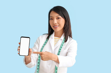 Female Asian nutritionist pointing at mobile phone on blue background