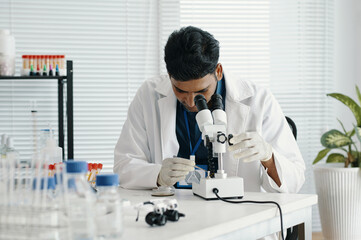 Scientist wearing lab coat concentrating on analyzing samples using microscope in laboratory....