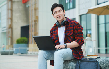 Portrait of a young Asian male student using a laptop on the street