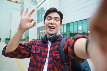 Portrait of a young Asian male student using his phone to take a selfie on the street
