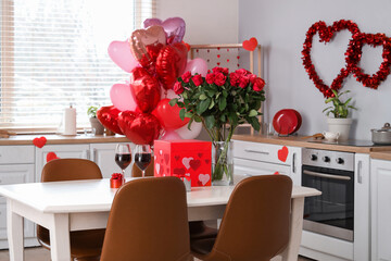 Dining table with bouquet of roses, wine glasses and gift boxes in light kitchen. Valentine's Day celebration