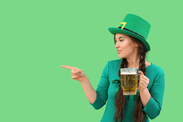 Young woman with beer pointing at something on green background. St. Patrick's Day