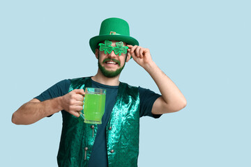 Young man in leprechaun hat and decorative glasses in shape of clover with green beard holding...