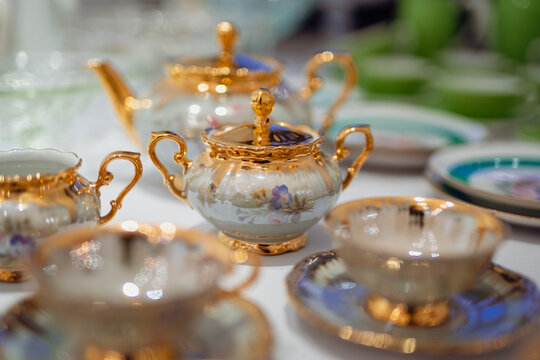 Close-up of vintage porcelain teapots and cups with gold detailing and floral designs, elegantly arranged on a table
