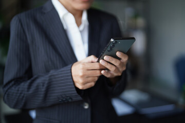 Asian businesswoman in suit standing using smartphone checking email
