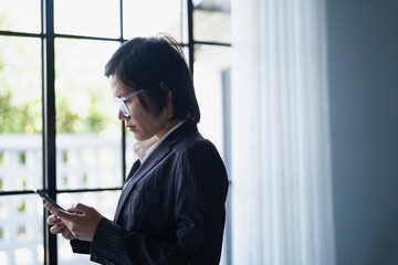 Asian businesswoman in suit standing using smartphone checking email