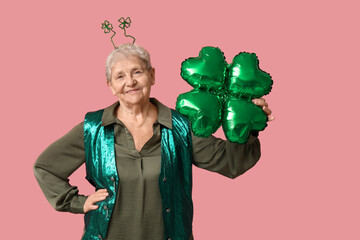 Senior woman in headband with air balloon in shape of clover on pink background. St. Patrick's Day celebration