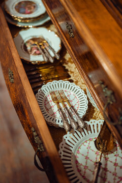 Vintage cutlery and decorative plates in an open antique wooden drawer, showcasing timeless elegance and craftsmanship