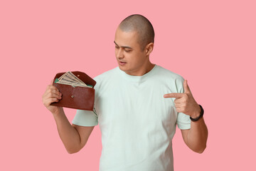 Young man pointing at wallet with money on pink background