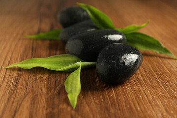 Spa stones and green leaves on wooden table, closeup
