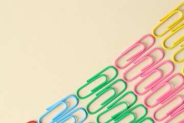 Colorful paper clips on beige background, flat lay. Space for text