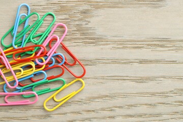 Many colorful paper clips on wooden table, top view. Space for text